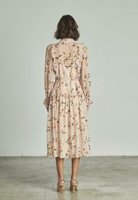 Vestido midi floral con un fondo rosa pálido, detalles de volantes, mangas largas y cintura ceñida, combinado con sandalias de tacón a juego.