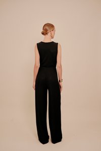 Černý bezrukávový overal s kalhotami širokých nohavic, hladkou texturou a přiléhavým pasem, pohled zezadu na neutrálním pozadí.
