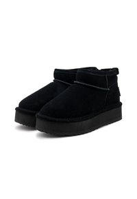 Botas de tobillo de ante negro con una suela de goma negra gruesa, que presentan un diseño sencillo y una textura suave, con un pequeño lazo en la parte trasera.