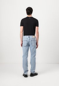 Camiseta negra de manga corta combinada con jeans de mezclilla azul claro. Los jeans tienen bolsillos traseros y una etiqueta de marca en la cinturilla. Calzado negro.