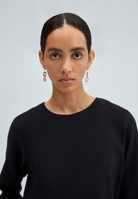 Sort langærmet bluse med rund halsudskæring, parret med guldøreringe i kæde-design. Glat tekstur og minimalistisk design.