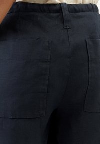 Pantalones de lino azul marino oscuro con grandes bolsillos de parche, una cinturilla elástica y un ajuste estructurado y casual. La textura parece suave y transpirable.