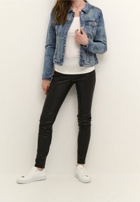 Jeansjacka i ljusblått med knappar, ihop med svarta, åtsittande läderbyxor och vita sneakers. Modell poserar med en hand på höften.