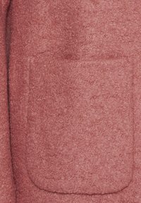 Gros plan sur un tissu en laine rose texturé avec une poche carrée cousue dessus.