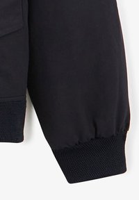 Manche de sweat-shirt noir avec un poignet côtelé texturé, tissu lisse et coupe ajustée pour un confort et une liberté de mouvement.