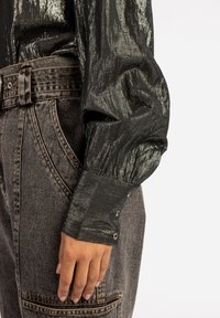 Zwarte metallic langemouwenshirt met een gestructureerde afwerking en opgetrokken mouwen, gecombineerd met hooggeprijsde donkergrijze jeans met contrasterende stiksels.