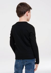 Schwarzes Langarmshirt aus Baumwolle mit Rundhalsausschnitt, körperbetonter Passform und glatter Oberfläche, kombiniert mit blauen Jeans.
