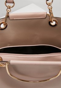 Sac à main en cuir rose avec intérieur beige, ferrures dorées et poche zippée. Présente un design structuré et une poignée courte et circulaire.