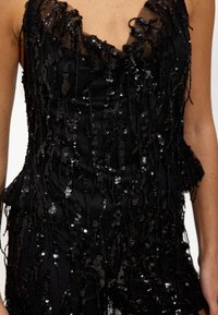 Top negro sin mangas con lentejuelas negras en capas y detalles con flecos, con escote transparente y ajuste estructurado.