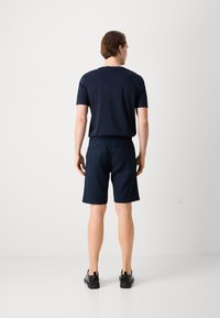 T-shirt di cotone blu navy e pantaloni shorts abbinati a lunghezza ginocchio, con vita elastica e due tasche posteriori, indossati con scarpe nere.