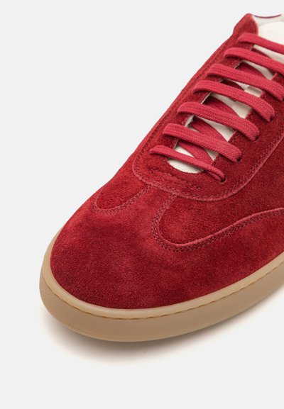 Baskets en daim rouge avec tige texturée, design incurvé, lacets assortis et une semelle en caoutchouc beige durable. Détails de couture accentués visibles.