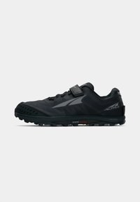 Black trail running shoe with a textured upper, toe bumper, and reinforced heel. Features a lacing system with a Velcro strap and rugged outsole.