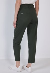 Pantaloni tapered verde scuro realizzati in tessuto leggero, dotati di due tasche posteriori e una vita alta, abbinati a sneakers bianche.