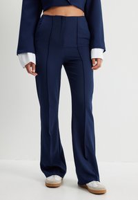 Pantalons taille haute bleu marine avec un design évas�é, dotés de plis avant et d'une texture de tissu lisse, associés à des manches blanches à revers.
