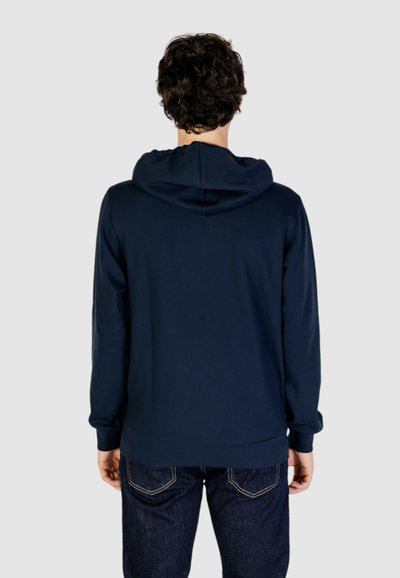 Felpa blu navy con tessuto testurizzato, una grande cappuccio e polsini a coste. Abbinata a jeans in denim scuro con cuciture a contrasto.