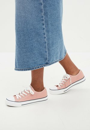 Zapatillas de lona rosas con cordones y punteras blancas, que cuentan con rayas marinas a lo largo de la suela. Combinadas con una falda de mezclilla azul.