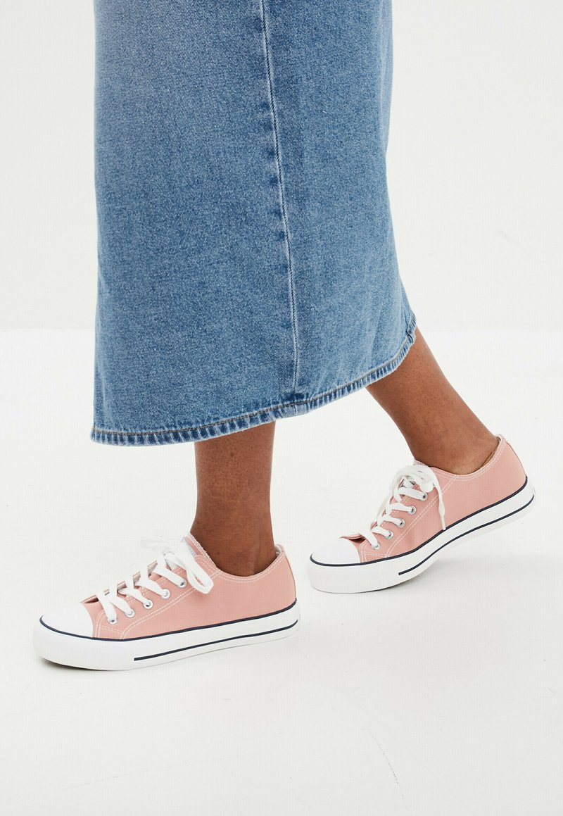 Sneaker di tela rosa con lacci e punte bianchi, caratterizzati da righe blu lungo la suola. Indossati con una gonna di jeans blu.