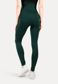 Leggings verdes de cintura alta hechos de tela elástica. Presentan una textura suave y un diseño ajustado. Combinados con zapatillas deportivas blancas.