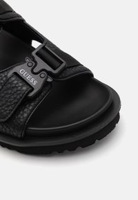 Sandali neri con tomaia testurizzata, suola nera spessa, cinturino regolabile con fibbia e logo del marchio impresso sul cinturino.