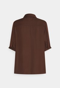 Brun skjorta med krage, korta ärmar och uppvikta ärmslut. Slät textur med rak bakdesign och inga synliga mönster eller accenter.