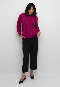 Pullover in magenta lavorato a maglia con motivo a onde, scollatura a girocollo e maniche lunghe, abbinato a pantaloni neri a sigaretta e décolleté neri a punta.