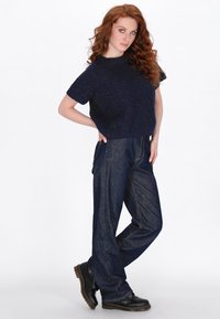 Marineblauw gebreid cropped sweater met korte mouwen, gecombineerd met een losse donkere spijkerbroek en zwarte veterschoenen. Soepele textuur en casual ontwerp.