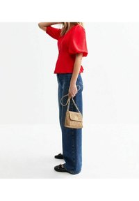 Rød tekstureret top med pufærmer, mørkeblå brede jeans, og en lille vævet guldhåndtaske, parret med sorte flade sko.