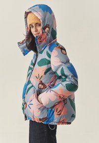 Puffjakke med et blåt, pink og grønt blomsterprint. Har høj krave og lynlås, samt en hyggelig strikket orange hue.