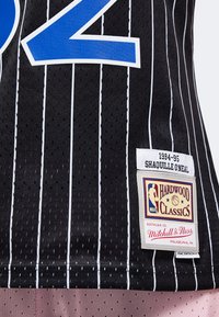 Nahaufnahme eines schwarzen Basketball-Trikots mit weißen Nadelstreifen, blauer Teilnummer und Aufnähern mit der Aufschrift 1994-95 Shaquille O’Neal und Hardwood Classics.