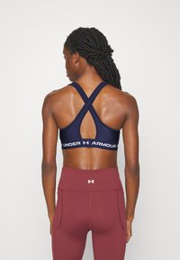 Marine sports-bh med kryssrygdesign, med en hvit "Under Armour" logo på båndet. Brukt med høyt liv maroon tights.