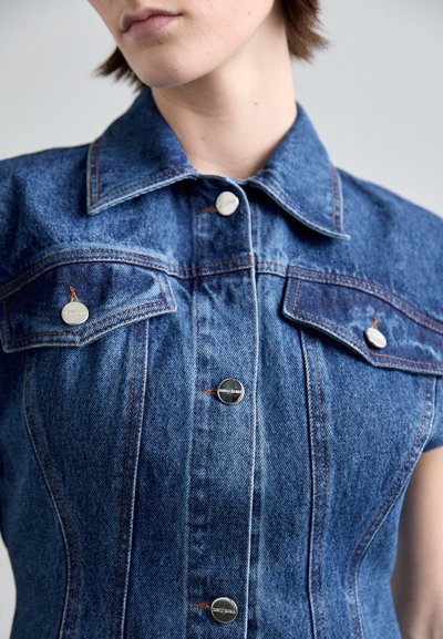 Rochie din denim cu guler, închidere cu nasturi, două buzunare pe piept și cusături contrastante de culoare portocalie. Materialul este denim albastru cu o textură netedă.