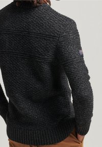 Dunkelgrauer, gestrickter Pullover mit einem strukturierten Muster, gerippten Bündchen und Saum. Enthält ein kleines Logo-Label auf dem linken Ärmel.