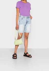 Fialové tričko s krátkým rukávem, světle modré džíny krátké kalhoty s třásněmi, černé sandály a malá kabelka s embosovaným krokodýlím vzorem v zelené barvě.