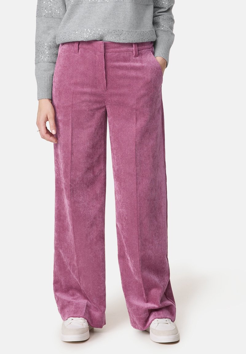 Pantalons en velours côtelé roses à jambes larges avec des côtes verticales et des poches latérales, associés à un pull texturé gris clair et des baskets blanches.