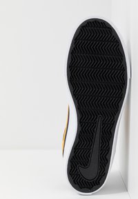 Musta kumipohja herringbone-kuviolla, kontrastivalkoinen välipohja ja värilliset sivustukset oranssina ja keltaisena.