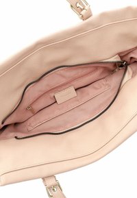 Light pink leather handbag interior featuring a zip pocket and a flat compartment, smooth texture, seamless design, and gold hardware accents.