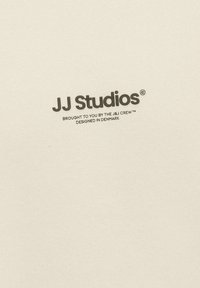 Cream cotton fabric featuring the text "JJ Studios" in black, along with smaller branding details, presented in a simple logo design.