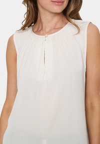 Blusa senza maniche color avorio con scollatura arricciata, caratterizzata da un dettaglio centrale con bottone, tessuto morbido e leggero per il massimo comfort.