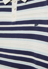 Polo en tricot rayé avec des rayures horizontales bleu marine, blanc et bleu clair, et trois boutons blancs sur la patte de col.