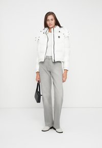 White puffer jacket with a cropped design, black zipper, and snap buttons, paired with light gray wide-leg jeans and a small black bag.