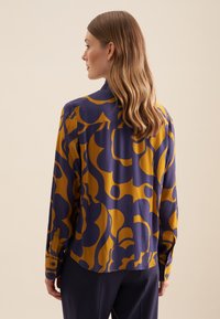 Langarmhemd met een paars en mosterdgeel geometrisch patroon, gemaakt van een gladde stof. Voorzien van knoopmanchetten en een klassieke kraag.