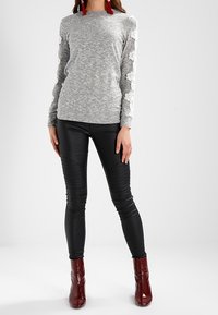 Grå långärmad topp med texturerad tyg och blommig spetsdetaljer på ärmarna, matchad med svarta läderbyxor och vinröda ankelstövlar.