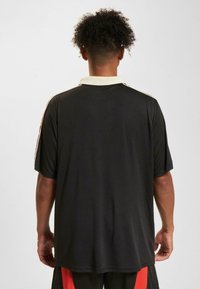 Tricou polo negru cu guler crem și dungi accent roșii pe umeri, având mâneci scurte și o croială lejeră.