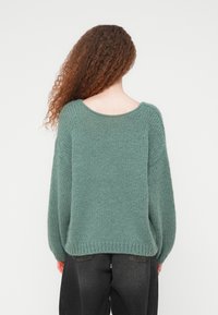 Πράσινο πλεκτό πουλόβερ με άνετη εφαρμογή, φαρδιές μανσέτες και σχεδιασμό με χαμηλωμένους ώμους. Μαλακή υφή με σχήμα λαιμού scoop στο πίσω μέρος.