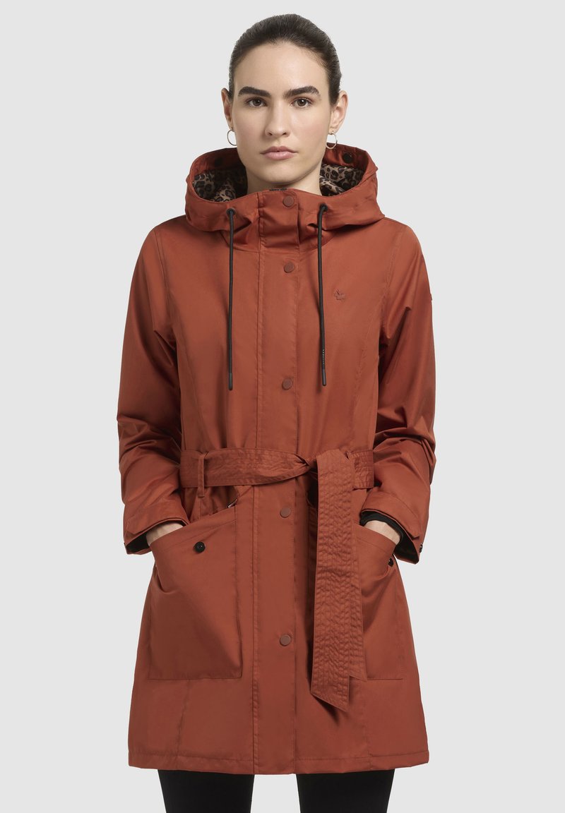 Waterafstotende roestkleurige jas met een trekkoord capuchon, riem en grote voorzakken. Gevoerd met een luipaardpatroon. Gladde textuur.