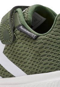 Grüne Netzsneaker mit verstärkter Zehenpartie, weißen Streifen und schwarzer Markenkennung auf der Zunge. Strukturierter Obermaterial für Atmungsaktivität.