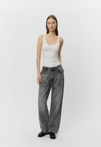 Jeans grigi larghi con una texture scolorita, abbinati a un top aderente bianco. I jeans presentano un classico design a cinque tasche.