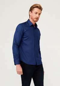 Marineblauwe blouse met knoopsluiting, gemaakt van een gladde stof, met een gestructureerde kraag en lange mouwen. De blouse heeft een slim-fit ontwerp.