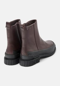 Mörkbruna läderankelboots med svarta texturerade tjocka sulor och sidodragkedjor, visade från baksidan och vinklade något åt höger.