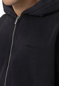 Manta escura com capuz azul marinho, apresentando uma textura suave, fecho frontal com zipper e logo "PEGADOR" em relevo no peito.